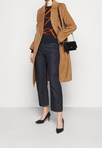 Camel wool-blend coat, black graphic sweater with orange lines, dark jeans, and black pointed-toe heels. Accessory: small black handbag.