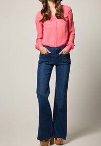 Rosa långärmad blus med knapplist fram, matchad med mörkblå utsvängda jeans och bruna träklackade plattformsskor.