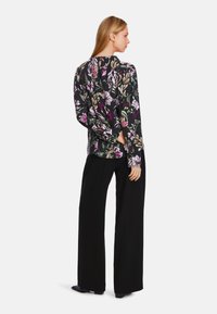 Lang�ärmliges Oberteil mit floralem Muster in Schwarz, das bunte Blumen zeigt. Kombiniert mit hochtaillierten, weiten schwarzen Hosen.