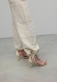 Crème linnen cargo broek met zakken, gecombineerd met nude sandaaltjes met hoge hakken en een vierkante neus en flared hak.