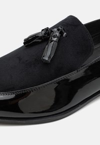 Mocassins noirs en suede et cuir verni. Quincaillerie à pompon noir remarquable et finition lisse et brillante.
