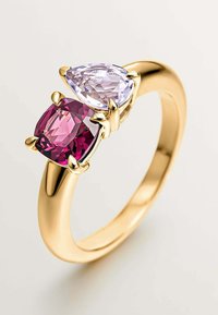 Anillo de oro que presenta dos piedras preciosas: una piedra de color púrpura claro en forma de pera y una piedra de color rosa profundo en corte cojín, engastadas en engastes de garra.
