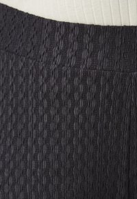 Black textured fabric with a wavy pattern; features a wide waistband; material appears lightweight and slightly elastic.
