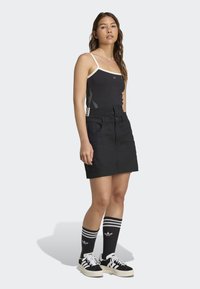 Zwarte katoenen rok met elastische tailleband, gecombineerd met een zwarte tanktop met een witte rand en een vlamgrafiek. Zwart-witte sneakers met gestreepte sokken.