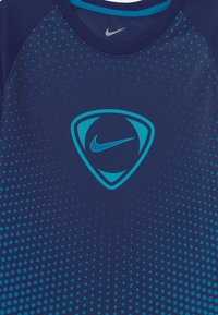 Tmavě modré sportovní tričko se vzorem modré gradientní tečky. Centrální logo je abstraktní design se světle modrým Nike swushem.