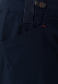 Tmavě modré kalhoty z lehké tkaniny s texturovaným pasem, diagonálním švem kapsy a kontrastním červeným prošitím.