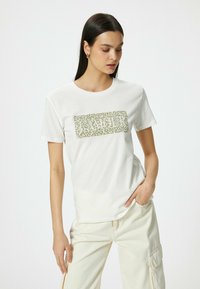 Hvid bomulds T-shirt med et leopardprint grafisk design i beige og grønne nuancer, med en klassisk rund hals og korte ærmer.