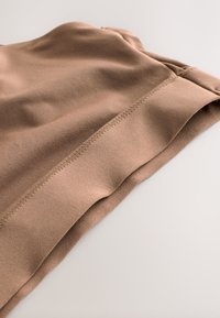 Nahaufnahme eines gefalteten braunen Kleidungsstücks mit glatter Stoffstruktur und sauberer Naht entlang der Naht auf einer hellen Oberfläche.
