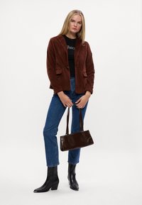 Brun kordfløjl blazer med knaplukning, parret med sort top, blå jeans og brun håndtaske. Sorte spidse støvler fuldender looket.