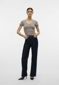 Ljusgrå åtsittande topp och högmidjade mörkblå jeans med raka ben. Modellen bär svarta klackskor med en ren design.