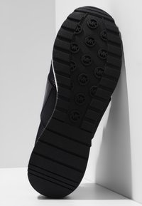 Suola di sneaker nera con un evidente motivo di battistrada, che include loghi circolari e scanalature orizzontali per una migliore aderenza. Realizzata in materiale gommoso.