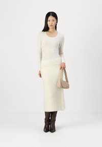 Pull en maille légère et jupe crème texturée, complétés par des bottes marron jusqu'aux genoux et un sac à main beige. Design simple et élégant avec des tons neutres.