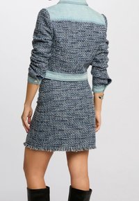 Sukienka z tkanego tweedu w kolorze granatowym i jasnoniebieskim, z górną częścią z denimu, dopasowaną talią, frędzlowanym dołem oraz długimi, marszczonymi rękawami.