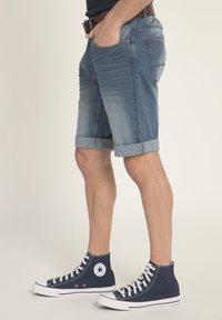 Shorts in denim di colore azzurro chiaro, con orlo arrotolato e tasche frontali, abbinati a sneakers alte blu navy. Texture liscia e design casual.