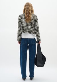Cropped sako s černobílým vzorem houndstooth přes bílou košili, v kombinaci s džínami s vysokým pasem a černou kabelkou.