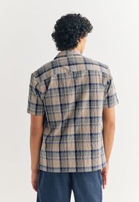 Short-sleeve plaid shirt in beige, blue, and navy. Lightweight fabric with a boxy cut, featuring a camp collar and back yoke detail.