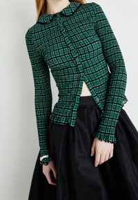 Groene geruite overhemd met lange mouwen en een kraag, voorzien van knopen aan de voorkant, gerimpelde mouwen en een getailleerd ontwerp, gecombineerd met een zwarte rok.