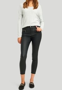 Svarta byxor i konstläder med smal passform, med dragkedjor i framfickorna och en slät textur. Styling med en ljusgrå långärmad topp.