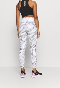 Leggings de sport PUMA avec un motif serpent blanc et gris, dotées d'une taille haute et d'un matériau extensible et lisse. À associer avec des baskets noires.