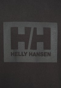 Tissu noir affichant un logo rectangulaire gris avec « HH » et « Helly Hansen » en lettres noires en gras, présentant une texture lisse.