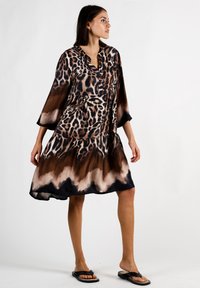 Leopardenmuster-Kleid aus seidig-weichem Stoff mit 3/4-Rüschärmeln. Es besitzt einen gestuften Rock, einen Schwarz-Braun-Gradienten und einen lässigen Schnitt. Schwarze Sandalen dazu getragen.