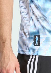 Bílý sportovní dres s modrým hvězdicovým vzorem, s černým logem FIFA a číslem "23" na dolním levém rohu. Černé šortky s bílými pruhy.