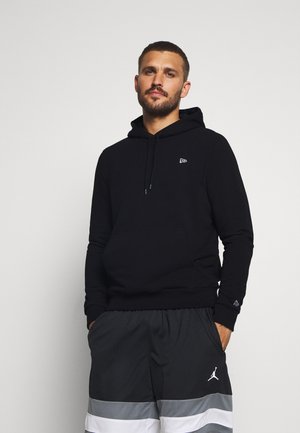 Felpa nera in cotone con tasca frontale e un piccolo logo, abbinata a pantaloni corti grigi con strisce bianche. Design semplice, vestibilità rilassata.