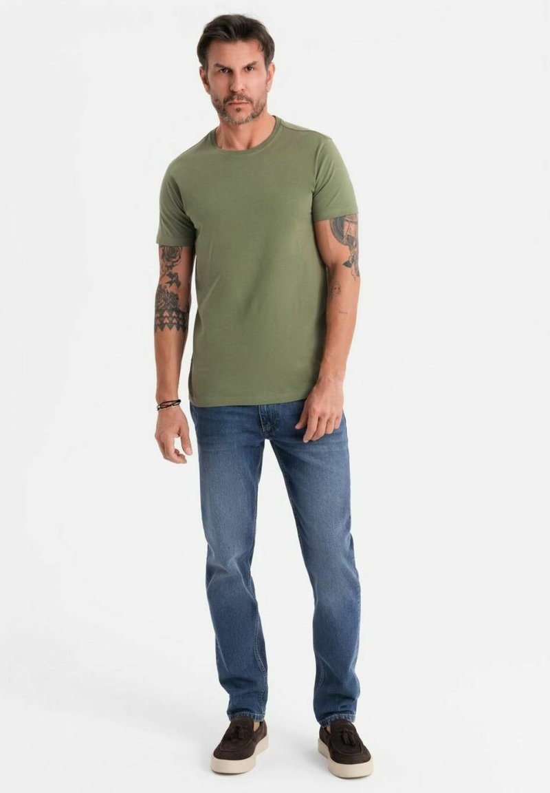 Camiseta de manga corta verde oliva, jeans de mezclilla azules y zapatillas marrones. La camiseta tiene un escote redondo; los jeans son de corte recto.