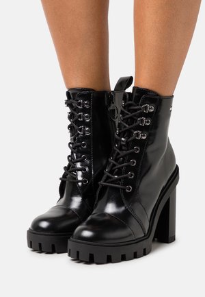 Zwarte leren enkelboots met een stevige platform en blokhak. Voorzien van een vetersluiting aan de voorkant, een zijrits en zilverkleurige hardwareaccenten.