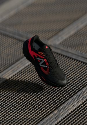 Czarno-czerwone buty biegowe z teksturowaną sieciową cholewką, okrągłym noskiem i kontrastowym białym logo. Posiadają miękką podeszwę oraz sznurowaną konstrukcję.