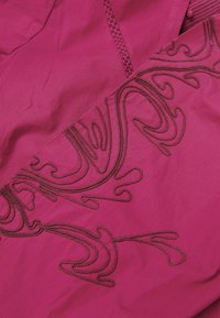Tessuto magenta con complessi ricami marroni e motivi ondulati, texture miste e dettagli decorativi a cucitura a reticolo.