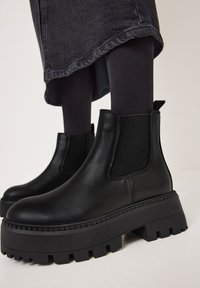 Botas negras de cuero hasta el tobillo con suelas gruesas y texturizadas, paneles laterales elásticos y un tirador, que cuentan con un acabado suave y un diseño resistente.