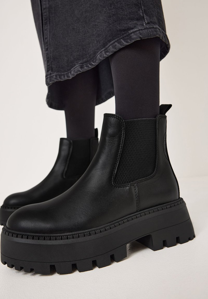 Botas negras de cuero hasta el tobillo con suelas gruesas y texturizadas, paneles laterales elásticos y un tirador, que cuentan con un acabado suave y un diseño resistente.