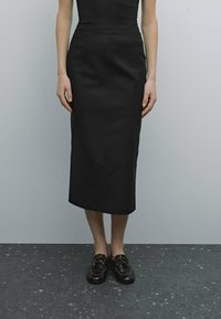 Jupe crayon noire en tissu lisse, au design ajusté avec un ourlet à mi-genoux. Associée à des chaussures noires à lacets.