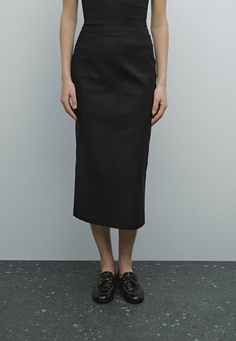 Jupe crayon noire en tissu lisse, au design ajusté avec un ourlet à mi-genoux. Associée à des chaussures noires à lacets.