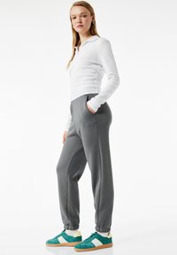 Hvid langærmet polo med krave, parret med grå sweatpants med sidelommer og elastiske manchetter; grønne sneakers med crème detaljer.