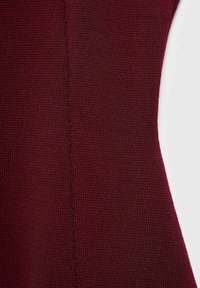 Burgundin neulosta, jossa on teksturoitu, ribbitty kuosi ja näkyviä ompeleita saumoissa, silkkinen kosketus.