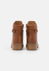 Botas de cuero marrón hasta el tobillo con una textura suave, dos hebillas laterales y un tacón apilado. La suela es de goma con un diseño de dibujos.