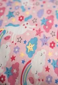Tela de algodón con un fondo rosa y patrones caprichosos de unicornios, nubes, estrellas y arcoíris en varios colores vibrantes.
