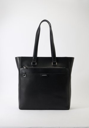Borsa tote in pelle nera testurizzata con due manici, tasca frontale con zip, anello metallico e logo Lacoste su sfondo bianco.