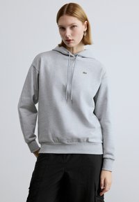 Hall halliga kapuutsiga dressipluus kängurutasku, ribaga mansettide ja väikese rohelise logoga. Pehme tekstuur ja lõdvestunud lõige. Sobitatud mustade pükstega.