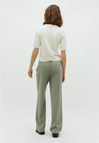 Camiseta blanca de manga corta combinada con pantalones holgados de talle alto en tono verde oliva, con una textura suave y sutiles bolsillos traseros.