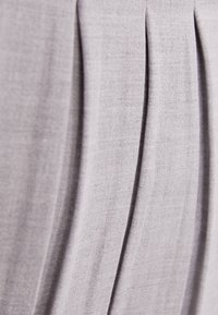 Skládaná látka v světle šedé barvě, s hladkou texturou a jemným leskem. Design obsahuje rovnoměrně rozložené vertikální záhyby pro strukturu.