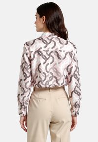 Long-sleeve blouse in light pink, featuring a wavy pattern in dark gray and white. Smooth fabric with a relaxed fit and button cuffs.