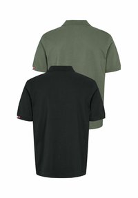 To ensfargede poloshorter sett bakfra, en svart foran en olivengrønn, hver med en liten rød og hvit etikett på ermet.