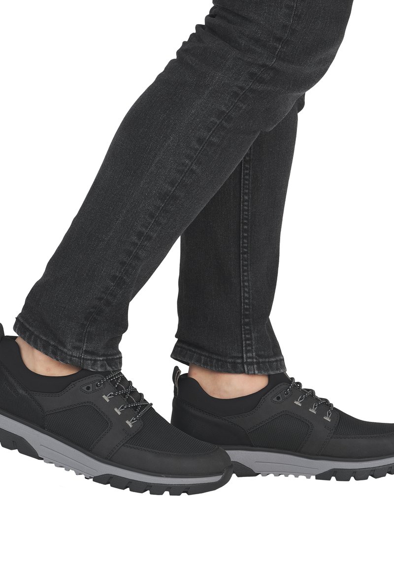 Des baskets de sport noires présentent un dessus en mesh et synthétique, une semelle en caoutchouc grise et des lacets contrastants. Associées à un jean noir slim.