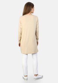 Tunique beige à manches longues avec un col rond, en tissu doux et à coupe droite, associée à un pantalon blanc ajusté et des baskets blanches.
