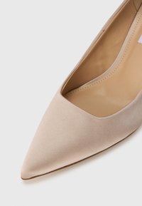 Γόβα με μυτερή μύτη σε γυμνό χρώμα, κατασκευασμένη από απαλό σατέν, με ομαλή υφή και χαμηλό κόψιμο στην περιοχή του ποδιού, με εσωτερικό σε ανοιχτό μπεζ χρώμα και λεπτό τακούνι.