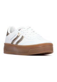 Zapatilla blanca con rayas metálicas doradas, parte superior de cuero texturizado, punta redondeada y suela de goma marrón con patrones de agarre. Cierre de cordones.