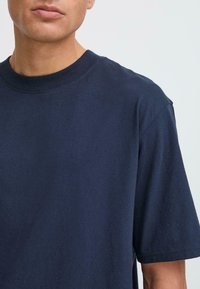 Marineblå t-skjorte med rund hals og korte ermer, i bomullsstoff, glatt tekstur og minimalistisk design. Ingen synlige mønstre eller detaljer.